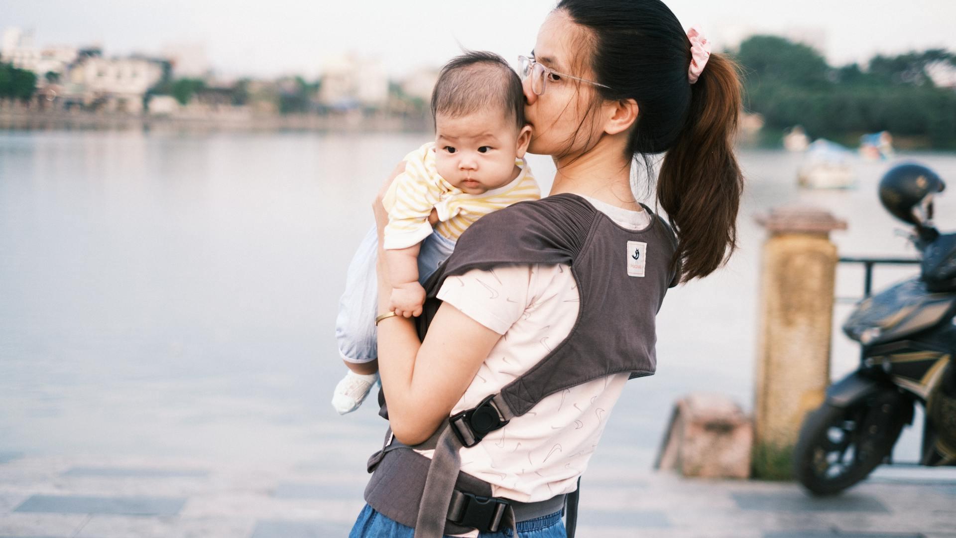 Mère portant son bébé en écharpe au bord de l'eau, coucher de soleil